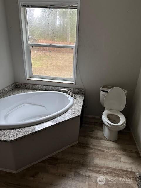 full bathroom featuring toilet, wood finished floors, a bath, and baseboards