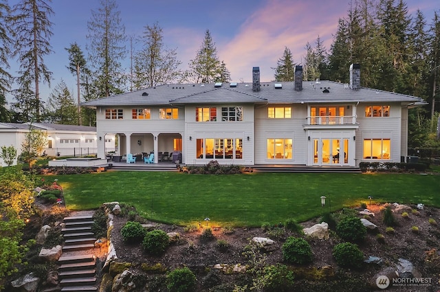 back of house featuring a patio, a lawn, a chimney, and a balcony