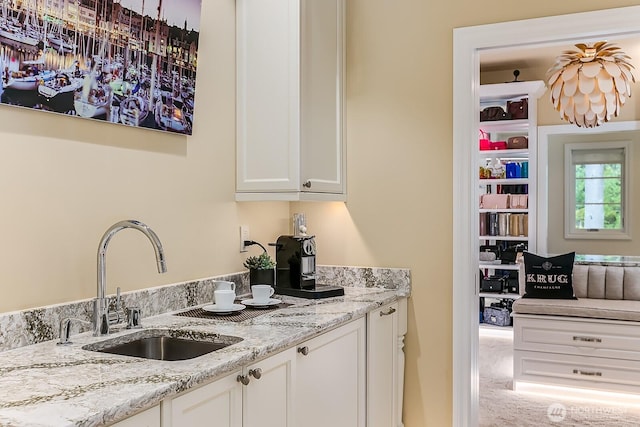 kitchen with light stone countertops, white cabinets, and a sink