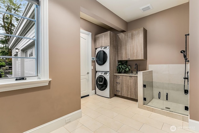 clothes washing area with cabinet space, baseboards, visible vents, stacked washer / drying machine, and a sink