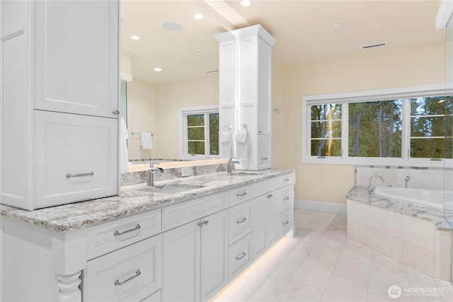 full bathroom with double vanity, tiled tub, a sink, and baseboards