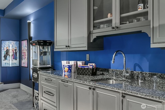 kitchen with glass insert cabinets, dark stone counters, a sink, and baseboards