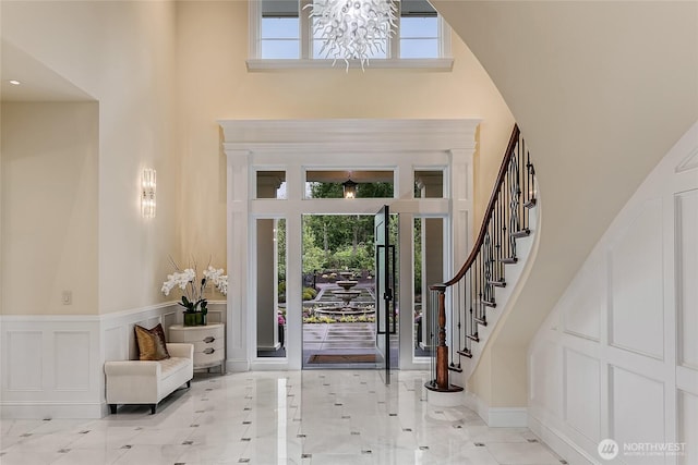 foyer entrance featuring stairs, a decorative wall, a towering ceiling, and a healthy amount of sunlight