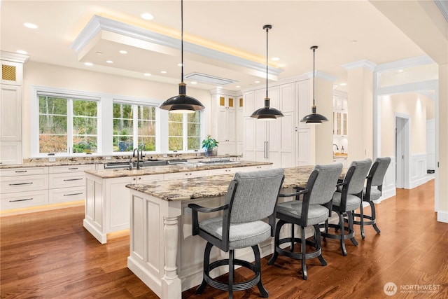 kitchen with light stone counters, glass insert cabinets, white cabinets, an island with sink, and wood finished floors