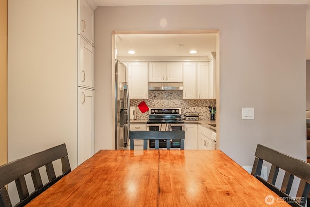 kitchen with white cabinets, stainless steel electric stove, under cabinet range hood, wooden counters, and backsplash