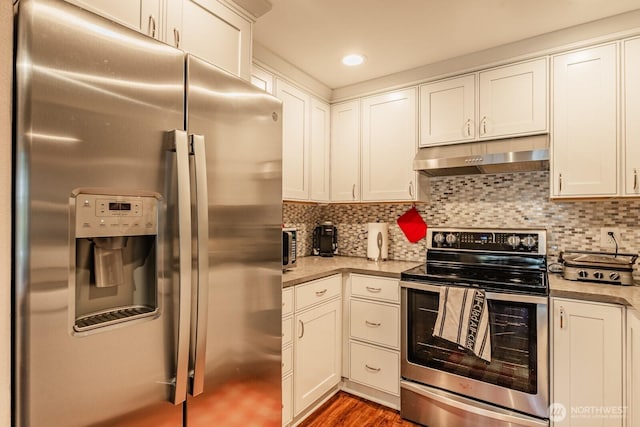 kitchen featuring under cabinet range hood, wood finished floors, white cabinets, appliances with stainless steel finishes, and decorative backsplash