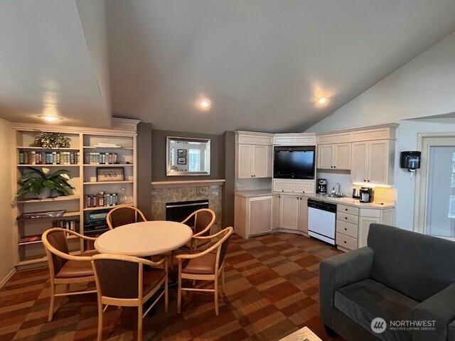 kitchen featuring a fireplace, lofted ceiling, light countertops, white cabinets, and white dishwasher