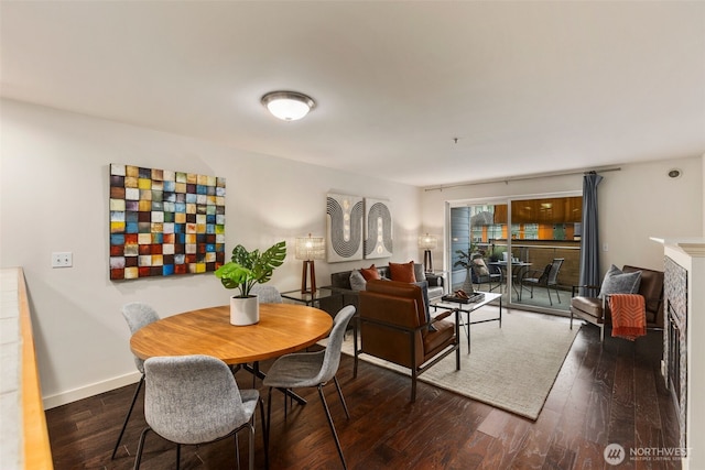 dining area featuring a fireplace, baseboards, and dark wood-style flooring