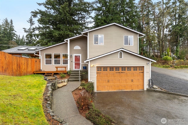 tri-level home with an attached garage, fence, aphalt driveway, and a front yard