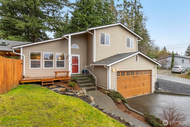 tri-level home with driveway, a shingled roof, an attached garage, fence, and a front lawn