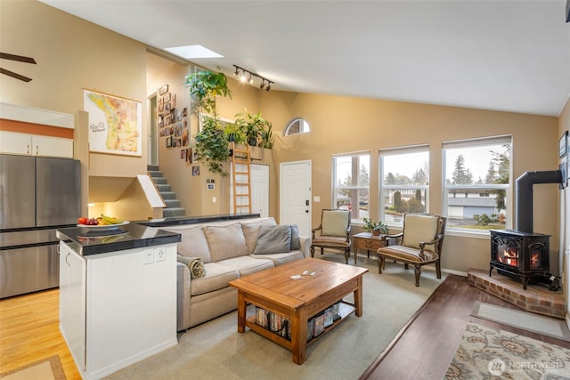 living area featuring stairway, a wood stove, rail lighting, vaulted ceiling, and light wood-type flooring