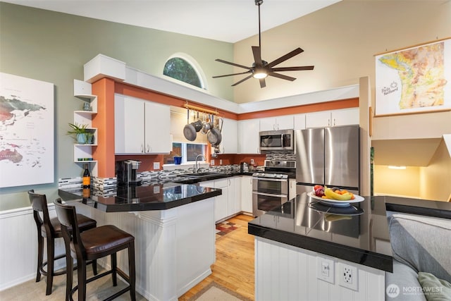 kitchen with white cabinets, dark countertops, a breakfast bar area, a peninsula, and stainless steel appliances