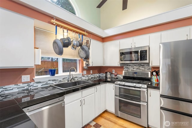 kitchen with decorative backsplash, white cabinets, dark countertops, appliances with stainless steel finishes, and a sink