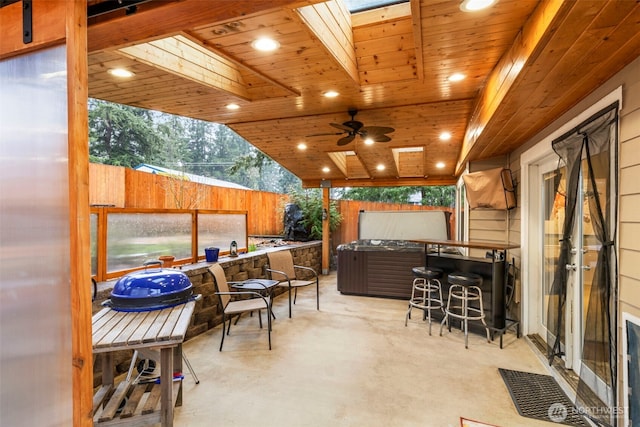 view of patio featuring exterior bar, a fenced backyard, a hot tub, and a ceiling fan