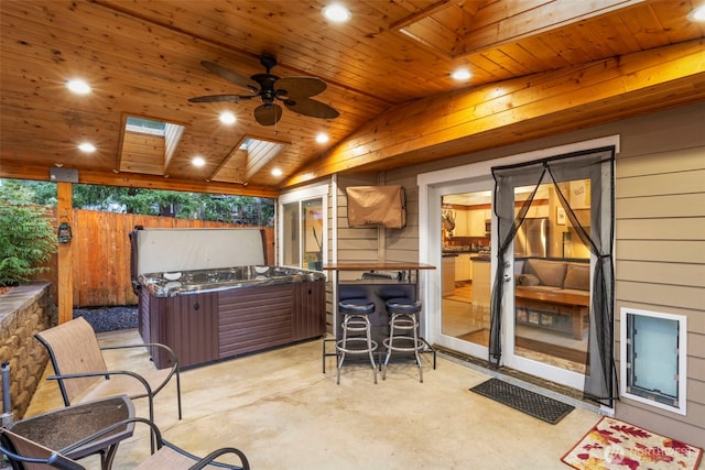 view of patio featuring exterior bar, a hot tub, fence, and a ceiling fan