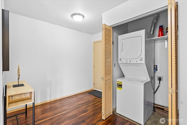 laundry area featuring stacked washer and dryer, dark wood finished floors, laundry area, and baseboards