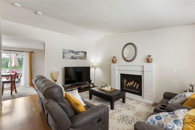 living area with a brick fireplace, vaulted ceiling, and light wood-style flooring