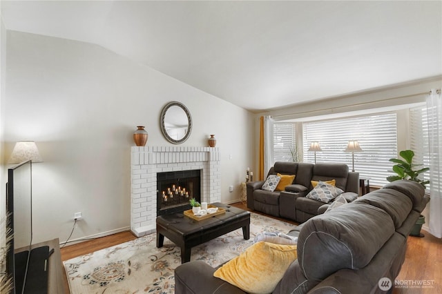 living area with lofted ceiling, a brick fireplace, wood finished floors, and baseboards