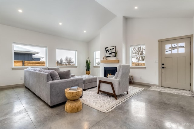 living room with high vaulted ceiling, recessed lighting, concrete flooring, a lit fireplace, and baseboards