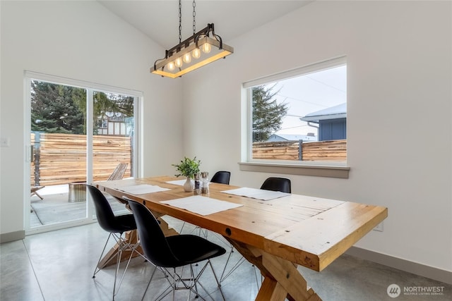 dining space with concrete flooring, lofted ceiling, plenty of natural light, and baseboards