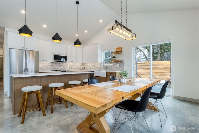 dining space with finished concrete floors, recessed lighting, high vaulted ceiling, and baseboards