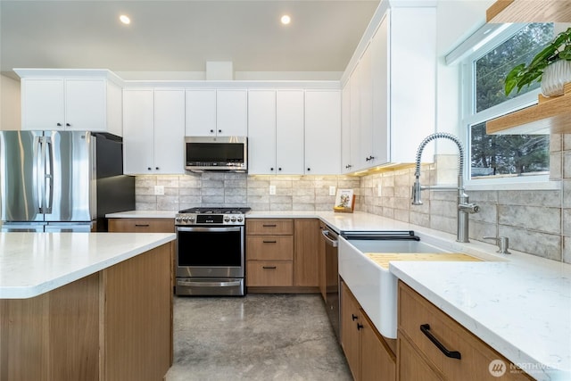 kitchen featuring light stone counters, a sink, white cabinets, appliances with stainless steel finishes, and decorative backsplash