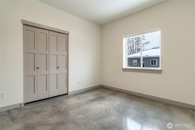 unfurnished bedroom with concrete flooring, a closet, and baseboards