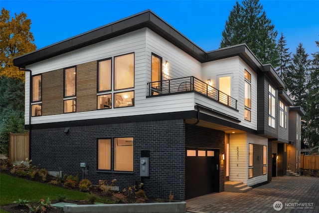 view of front of property featuring brick siding, decorative driveway, an attached garage, and a balcony