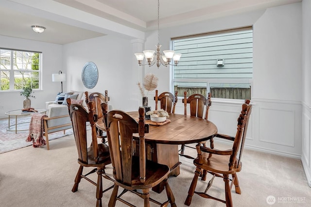 dining room featuring wainscoting, light carpet, a decorative wall, and an inviting chandelier