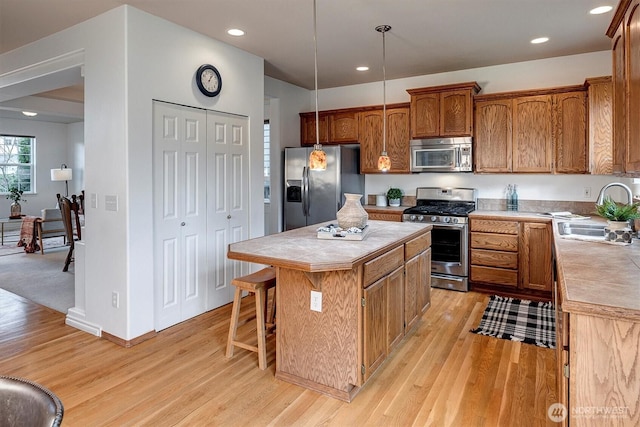 kitchen with a sink, appliances with stainless steel finishes, tile counters, a center island, and light wood finished floors