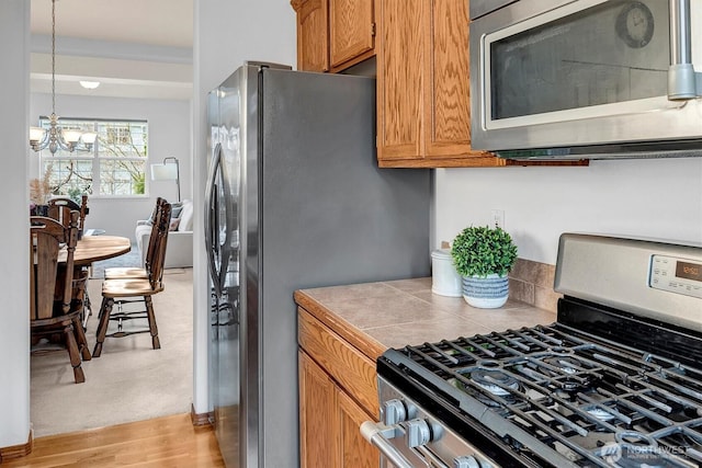 kitchen with tile counters, brown cabinetry, stainless steel appliances, light wood-style floors, and a chandelier