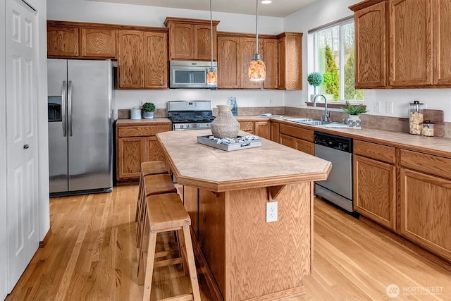 kitchen with a center island, appliances with stainless steel finishes, brown cabinetry, a sink, and light wood-type flooring