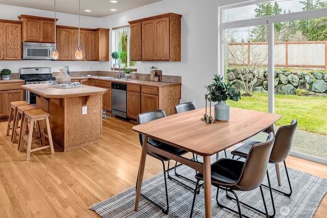 kitchen with stainless steel appliances, light wood-style flooring, brown cabinetry, a kitchen island, and a sink