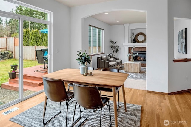 dining area with a glass covered fireplace, baseboards, visible vents, and light wood finished floors