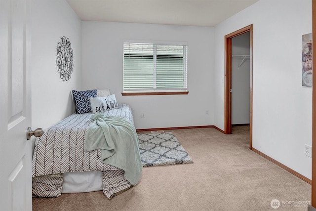 carpeted bedroom with a walk in closet and baseboards