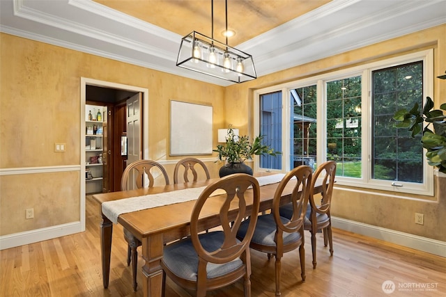 dining area featuring light wood-style flooring, baseboards, a raised ceiling, and crown molding