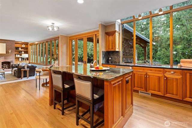 kitchen featuring a fireplace, visible vents, light wood-style floors, a sink, and dark stone countertops