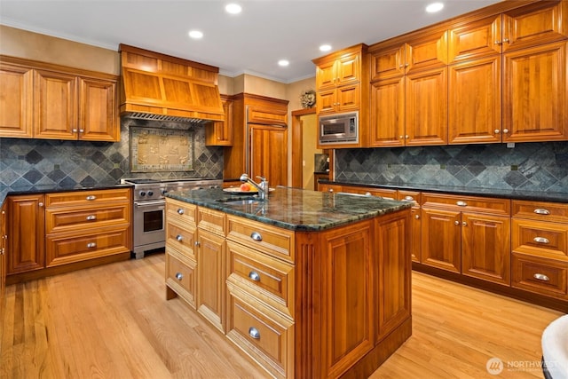 kitchen with brown cabinets, custom exhaust hood, stainless steel appliances, light wood-style flooring, and a sink