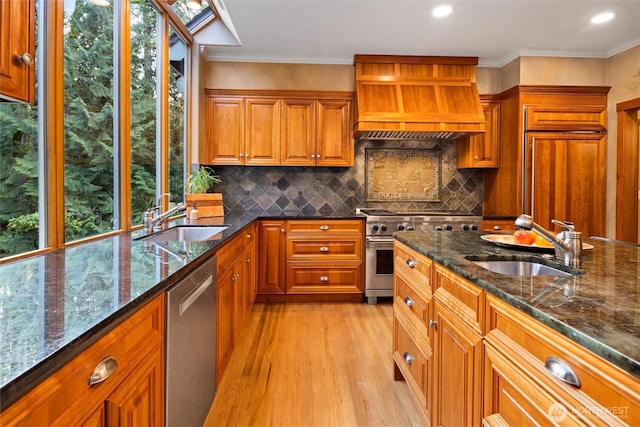 kitchen featuring custom range hood, high quality appliances, brown cabinets, and a sink