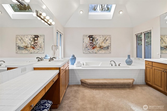 full bathroom featuring a garden tub, vaulted ceiling with skylight, two vanities, and a sink