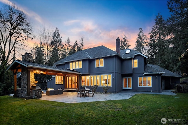 back of property at dusk with a chimney, a patio area, and a lawn