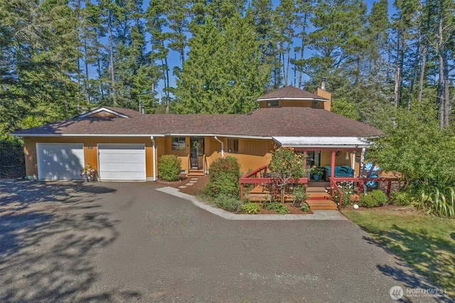 view of front of home with covered porch, driveway, a chimney, and an attached garage