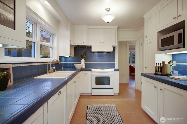 kitchen with white range with electric stovetop, tile countertops, stainless steel microwave, white cabinetry, and a sink