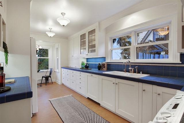 kitchen with tile countertops, backsplash, glass insert cabinets, white cabinetry, and a sink