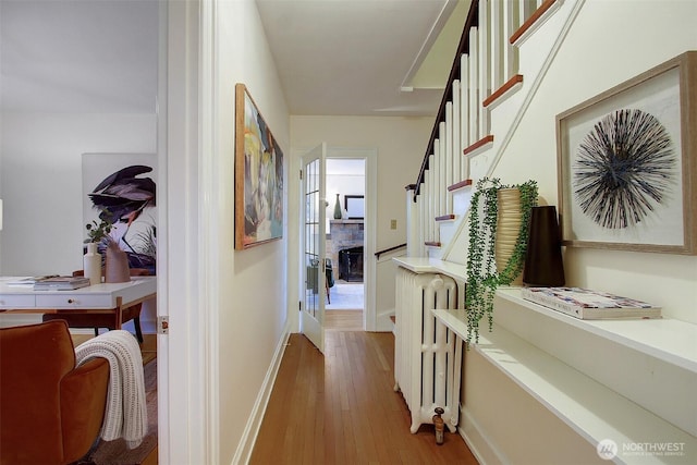 corridor with light wood-type flooring, radiator, stairway, and baseboards