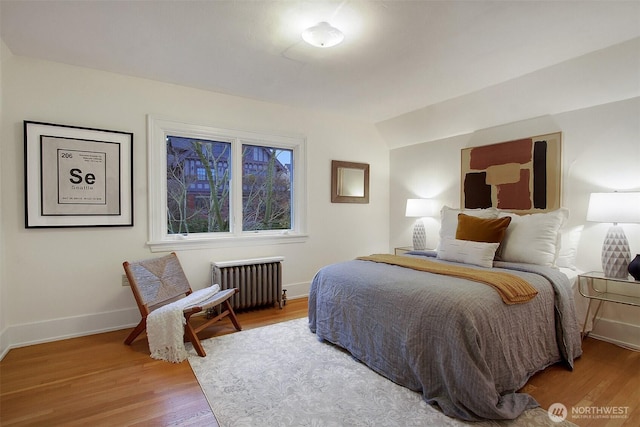 bedroom with radiator heating unit, wood finished floors, and baseboards