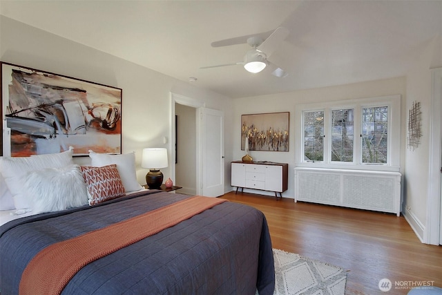 bedroom featuring a ceiling fan, baseboards, radiator heating unit, and wood finished floors