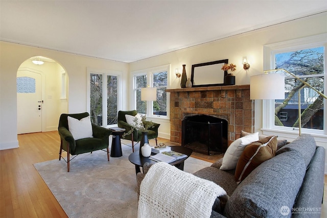 living room featuring a fireplace with flush hearth, arched walkways, and light wood finished floors