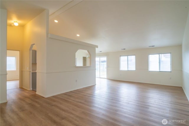 empty room featuring recessed lighting, arched walkways, baseboards, and wood finished floors