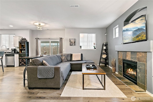 living area with light wood-style floors, visible vents, a fireplace, and baseboards